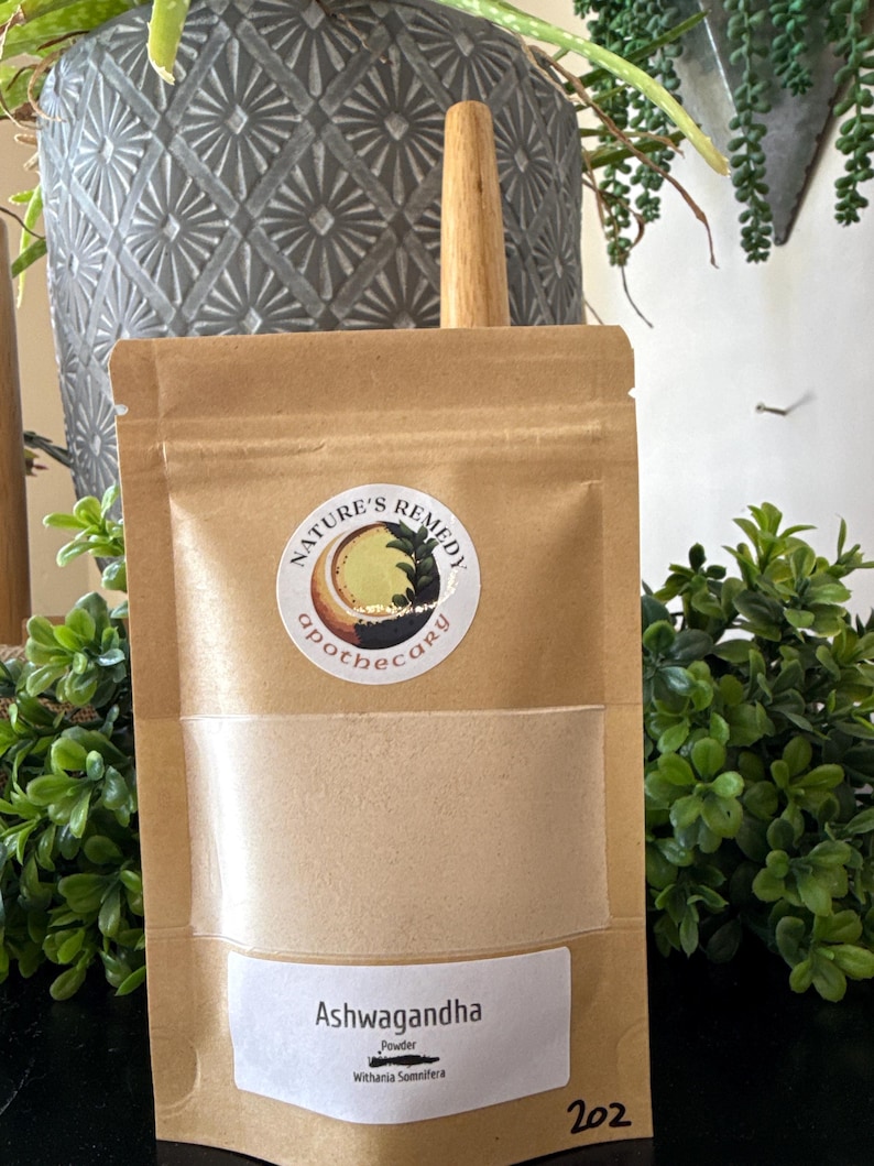 Puede incluir: Una bolsa de papel marr&oacute;n con una ventana transparente que contiene un polvo beige. La bolsa tiene una etiqueta blanca que dice "Ashwagandha Powder" y una pegatina circular con las palabras "Nature's Remedy Apothecary". El n&uacute;mero "202" est&aacute; impreso en la parte inferior derecha.