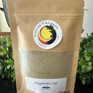 May include: A brown paper bag with a clear window containing a green powder. The bag has a white label that reads "Peppermint Leaf" and "1 oz." A circular sticker with the words "Nature's Remedy Apothecary" is on the bag.