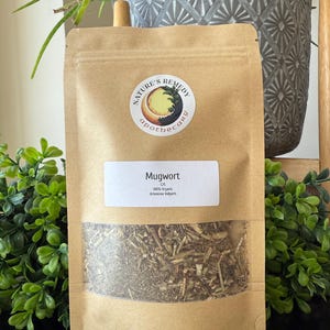 Könnte beinhalten: Ein brauner Papiersack mit einem transparenten Fenster, gefüllt mit getrockneten Kräutern. Der Beutel hat ein weißes Etikett mit der Aufschrift "Mugwort" und "100% Organic Artemisia Vulgaris". Ein runder Aufkleber mit den Worten "Nature's Remedy Apothecary" ist ebenfalls sichtbar. Der Beutel enthält 42.5 Gramm Produkt.