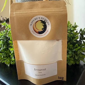 May include: A brown paper bag with a clear window containing white powder. The bag has a label that reads "Arrowroot Powder" and a sticker with the text "Nature's Remedy Apothecary". The bag contains 1 oz of powder.