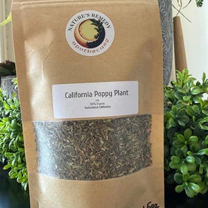 May include: A brown paper bag with a clear window, filled with dried green herbs. The bag has a label that reads "California Poppy Plant" and "100% Organic". The bag also has a sticker that says "Nature's Remedy Apothecary". The bag contains 1.5 oz of product.
