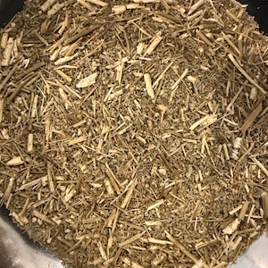 May include: Close-up of dried, chopped herbs and stems. The mixture is a blend of light brown and tan colors, with a variety of textures from thin, straw-like pieces to small, leafy fragments. The herbs are contained in a dark bowl.