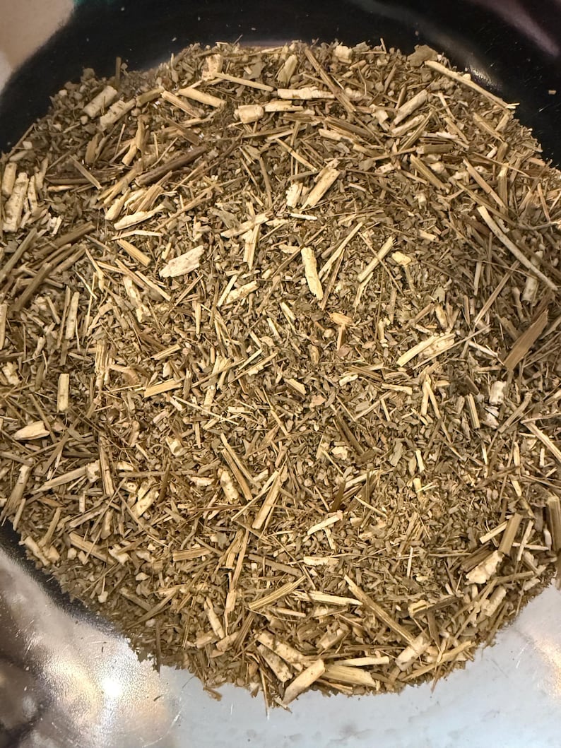 May include: Close-up of dried, chopped herbs and stems. The mixture is a blend of light brown and tan colors, with a variety of textures from thin, straw-like pieces to small, leafy fragments. The herbs are contained in a dark bowl.