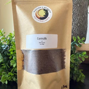 Könnte beinhalten: Ein brauner Papiertüte mit Maisseidentee. Die Tüte hat ein klares Fenster, das den Tee im Inneren zeigt. Die Tüte hat ein Etikett mit der Aufschrift "Cornsilk" und "100% Organic". Die Tüte hat auch einen Aufkleber mit der Aufschrift "Nature's Remedy Apothecary". Die Tüte ist 42.5 Gramm.