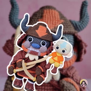 May include: Crocheted figures of characters from Avatar: The Last Airbender. The main figure is a brown and orange creature with large horns, holding a smaller Aang figure. The figures are handmade with detailed stitching and vibrant colors.