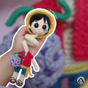 Op de afbeelding: Gehaakte Luffy-pop met een gele strohoed, zwart haar en een rood vest. De pop heeft een blauwe korte broek, bruine sandalen en een paarse bal. De tekst "La Chica Lunar" is zichtbaar.