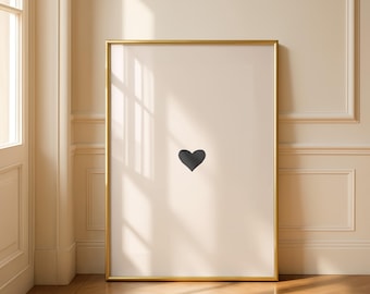 May include: A framed art print featuring a minimalist design. The artwork showcases a single, dark gray heart centered on a cream-colored background. The frame is a thin, gold color, adding a touch of elegance to the piece.