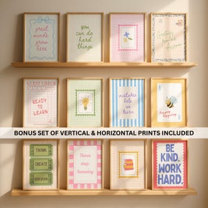 May include: A collection of twelve vertical wall art prints displayed on three wooden shelves. The prints feature various educational themes, pastel colors, and motivational text including "great minds grow here," "ready to learn," and "be kind, work hard."