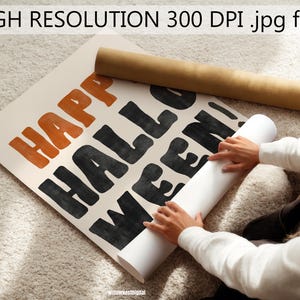Puede incluir: Un p&oacute;ster rectangular con el texto HAPPY HALLOWEEN! en letras negritas de estilo dibujado a mano. La palabra HAPPY est&aacute; impresa en naranja, mientras que HALLOWEEN! est&aacute; en negro sobre un fondo crema. Un tubo de cart&oacute;n marr&oacute;n est&aacute; cerca.