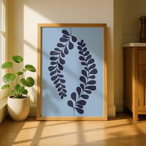 May include: A framed art print featuring a light blue background with a dark blue leaf design. The artwork is encased in a natural wood frame and rests on a wooden floor. A potted plant is visible in the corner.