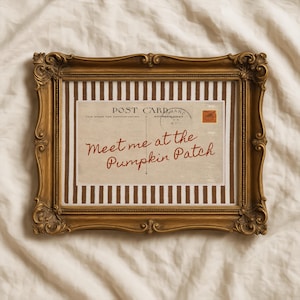 May include: A rectangular ornate gold frame containing a print of a vintage postcard with brown and white vertical stripes. The postcard features the text "POST CARD" and "Meet me at the Pumpkin Patch" in cursive red script with a small orange stamp.