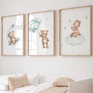 Puede incluir: Tres impresiones enmarcadas con ilustraciones de acuarela de un oso de peluche marrón. La primera impresión muestra al oso durmiendo en una luna creciente con estrellas. La segunda impresión muestra al oso sosteniendo globos. La tercera impresión muestra al oso sentado en una nube sosteniendo una estrella.