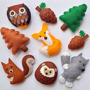 May include: Felt woodland animal ornaments, including an owl, fox, squirrel, hedgehog, pine trees, and pinecones. The ornaments are brown, orange, green, and gray.