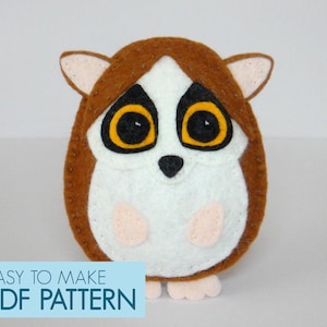 May include: A handmade felt lemur toy in brown, white, and tan. The lemur features large yellow eyes with black pupils, small ears, and a white face and belly. The text "EASY TO MAKE PDF PATTERN" is in a blue box.