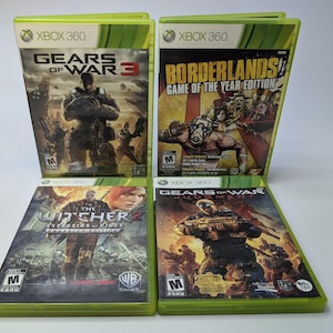 Puede incluir: Cuatro cajas de juegos de video para Xbox 360. Las cajas son verdes y presentan diferentes juegos: Gears of War 3, Borderlands Game of the Year Edition, The Witcher 2 Assassins of Kings Enhanced Edition y Gears of War Judgement.