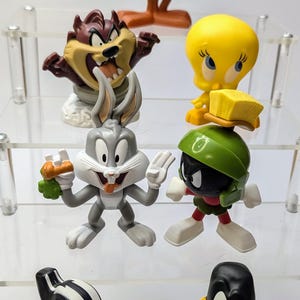 May include: A set of six Looney Tunes character figurines. The characters include Bugs Bunny, Daffy Duck, Tweety Bird, Road Runner, Sylvester the Cat, and Marvin the Martian. The figurines are made of plastic and are brightly colored.