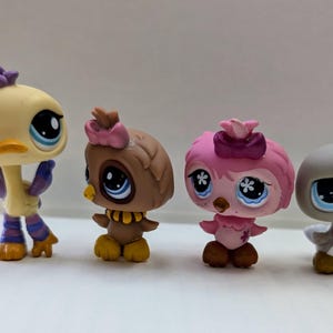 May include: Four small plastic toy animals, a yellow bird, a brown owl, a pink bird, and a gray bird. Each toy has large eyes and a cute expression.