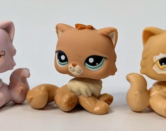 May include: Five colorful cat figurines. The cats are in various shades of cream, pink, and orange. Each cat has large, expressive eyes and is posed in a sitting position. The figurines are likely collectible toys, with detailed features and a playful design.
