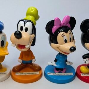 May include: Four plastic Disney character figurines: Donald Duck in blue, Goofy in orange, Minnie Mouse in blue, and Mickey Mouse in red. Each figurine has a base with the text "Walt Disney World Resort".