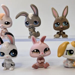 Puede incluir: Seis figuras de conejos de juguete de varios colores. Los conejos están en diferentes poses y tonos, incluyendo rosa, gris, marrón y blanco. Cada conejo tiene ojos grandes y orejas largas. Los juguetes son de plástico y probablemente artículos de colección.