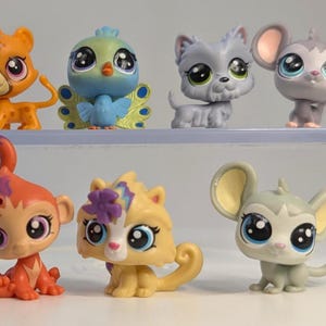 May include: A collection of colorful, stylized animal figurines. The assortment includes a cheetah, a bird, a dog, a monkey, a cat, and two mice. Each figure has large eyes and decorative accents.