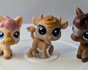 May include: Three small plastic toy animals. A brown and white cow with a gold glitter mane, a brown horse with a brown mane, and a light brown horse with a pink mane.