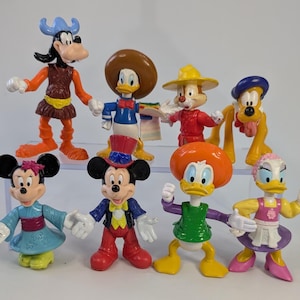 Peut inclure: Un ensemble de sept figurines en plastique représentant des personnages Disney, dont Dingo avec un casque viking, Donald avec un sombrero, Tic ou Tac avec un chapeau jaune, Pluto, Minnie en robe bleue, Mickey avec un haut-de-forme et deux autres canards.