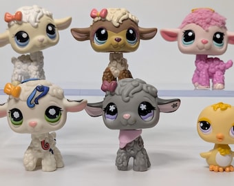May include: A collection of six colorful Littlest Pet Shop animal figurines. The figurines include sheep and a chick, each with large eyes and unique details. The sheep have bows and the chick has orange feet.