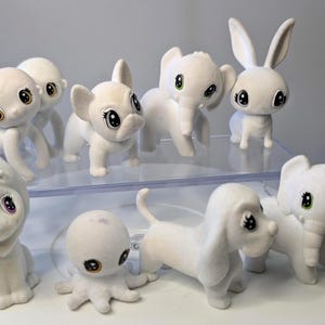 Puede incluir: Una colección de juguetes de peluche de animales blancos con ojos grandes. Los juguetes incluyen un león, un mono, un elefante, un cerdo, un conejo, un dachshund, un pulpo y otro elefante.