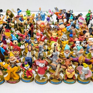 以下が含まれることがあります： ミッキーマウス、白雪姫、くまのプーさんなど、ディズニーキャラクターのフィギュアのコレクション。フィギュアはカラフルで詳細で、金色のベースが付いています。キャラクターは白い表面に配置されています。