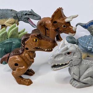 May include: A set of six dinosaur toys, including a grey and brown Tyrannosaurus Rex, a green Stegosaurus, a brown Triceratops, a grey Ankylosaurus, a blue Velociraptor, and a grey Baryonyx.