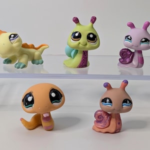 Puede incluir: Cinco figuras de animales coleccionables y coloridas. La colección incluye un lagarto amarillo y naranja, un insecto verde y morado, un caracol rosa, una seta naranja y un caracol melocotón. Cada figura tiene ojos grandes y expresivos.