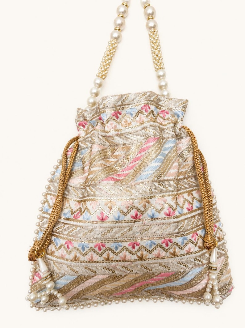 May include: An intricately embroidered drawstring bag with a cream-colored base, adorned with pink, blue, and gold threadwork. The bag features pearl-beaded handles and a pearl-trimmed drawstring closure. The bag's design includes floral and geometric patterns.