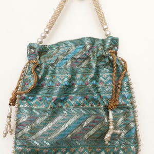 May include: A teal drawstring bag with a pearl beaded handle and trim. The bag is decorated with sequins and embroidered floral patterns in shades of blue, pink, and gold. The drawstring is gold, and the bag has a tassel with pearls.