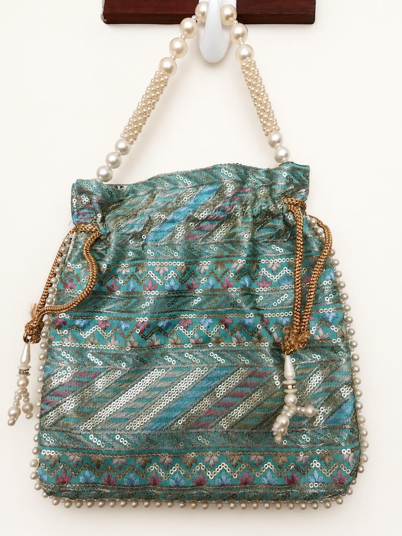 May include: A teal drawstring bag with a pearl beaded handle and trim. The bag is decorated with sequins and embroidered floral patterns in shades of blue, pink, and gold. The drawstring is gold, and the bag has a tassel with pearls.