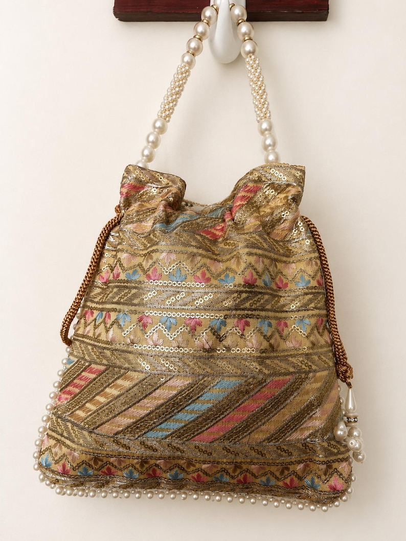May include: A gold-colored drawstring bag with intricate embroidery and sequin details. The bag features a pearl beaded handle and a pearl trim along the bottom edge. The design includes pink, blue, and red accents.