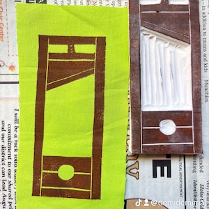 May include: A close-up of a green fabric with a brown print of a guillotine. The fabric is next to a brown and white print of a guillotine. The text "I will be a rock solid commitment to our shared principles, and our district can lead Augusta again" is visible on the fabric.