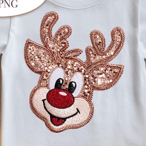 Könnte beinhalten: Weißes T-Shirt mit einem niedlichen Rentier-Design. Das Rentier hat paillettenbesetzte Geweihe, eine rote Nase und ein lächelndes Gesicht. Der Text "Cute Deer 1 PNG" befindet sich in einem weißen Oval. Ideal für die Weihnachtszeit.
