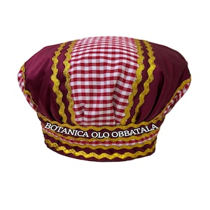 Puede incluir: Un sombrero a cuadros burdeos y blancos con ribete dorado y el texto "BOTANICA OLO OBBATALA". El sombrero tiene una copa redonda y un ala ancha, con ribete dorado. El sombrero es de tela.