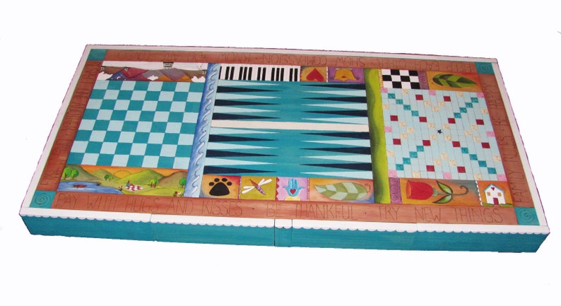 K&ouml;nnte beinhalten: Ein Holzspielbrett mit einer t&uuml;rkisblauen Oberfl&auml;che. Das Brett bietet mehrere Spiele, darunter Dame, Backgammon und ein Tic-Tac-Toe-artiges Spiel. Das Brett ist mit bunten bemalten Designs und dem Text "Say with hugs and kisses, be thankful, try new things" verziert.