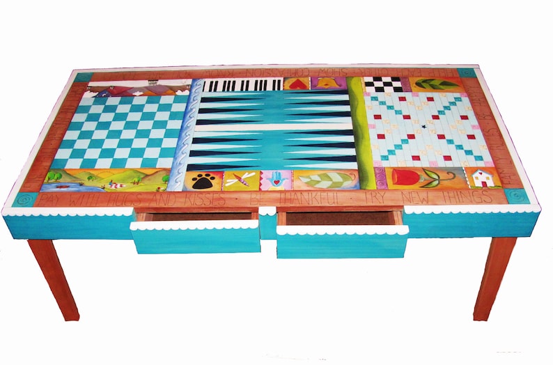 K&ouml;nnte beinhalten: Ein h&ouml;lzerner Spieltisch mit einem blau-wei&szlig;en Schachbrett, einem Backgammon-Brett und einem Tic-Tac-Toe-Brett. Der Tisch hat drei Schubladen mit einem wei&szlig;en, gewellten Rand und die Worte "By With Hugs And Kisses Be Thankful Try New Things" sind auf die Vorderseite gemalt.