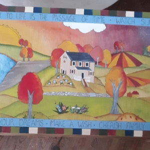 K&ouml;nnte beinhalten: Eine Holzkiste mit einem gemalten Bild eines Hauses in einer l&auml;ndlichen Landschaft. Die Kiste hat einen blau-gr&uuml;n-rot-wei&szlig; gestreiften Rand. Der Text auf der Kiste lautet: "Das Geheimnis des Lebens ist der Lauf der Zeit - Sonnenunterg&auml;nge beobachten - Tiere lieben - deinen Tr&auml;umen folgen - einen Wunsch machen - Familie sch&auml;tzen - ruhig sitzen - Frieden finden - die Natur genie&szlig;en."