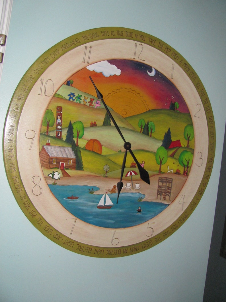 May include: A round wooden clock with a painted scene of a lake, hills, and a sunset. The clock face has Roman numerals and a green, yellow, and brown border with text that reads "The Gang That's All True Blue You Take The Pep From A Pepsi Cola You Take The Luck From A Lucky Strike You Take The Zip From A Talon Zipper You Take The Gleam From An Electric Light Electric Light And When You Put Them All Together With The Aid Of String And Skin And Get That Gang Mom Camp Arrowhead".