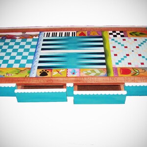 K&ouml;nnte beinhalten: Ein h&ouml;lzerner Spieltisch mit einem blau-wei&szlig;en Schachbrett, einem Backgammon-Brett und einem Tic-Tac-Toe-Brett. Der Tisch hat drei Schubladen und die Worte "By With Hugs and Kisses Be Thankful Try New Things" sind auf die Vorderseite gemalt.
