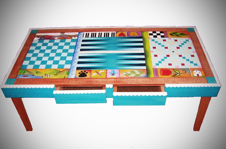 K&ouml;nnte beinhalten: Ein h&ouml;lzerner Spieltisch mit einem blau-wei&szlig;en Schachbrett, einem Backgammon-Brett und einem Tic-Tac-Toe-Brett. Der Tisch hat drei Schubladen und die Worte "By With Hugs and Kisses Be Thankful Try New Things" sind auf die Vorderseite gemalt.