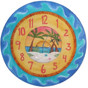 May include: A round wooden clock with a beach scene painted on the face. The clock has a blue and turquoise wave border and a rope-like design around the edge of the face. The numbers are in red and the hands are silver. The beach scene features palm trees, a sunset, and a sandy beach.