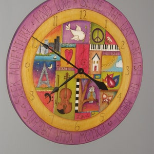 May include: A colorful wooden clock with a purple outer ring and a yellow inner ring. The clock face is decorated with various images, including a bird, a piano, a house, a violin, and an owl. The clock hands are black and the numbers are in white. The outer ring has the text "SEEK ADVENTURE FIND LOVE? SEIZE THE DAY? RELISH THE NIGHT? FOLLOW YOUR DREAMS".