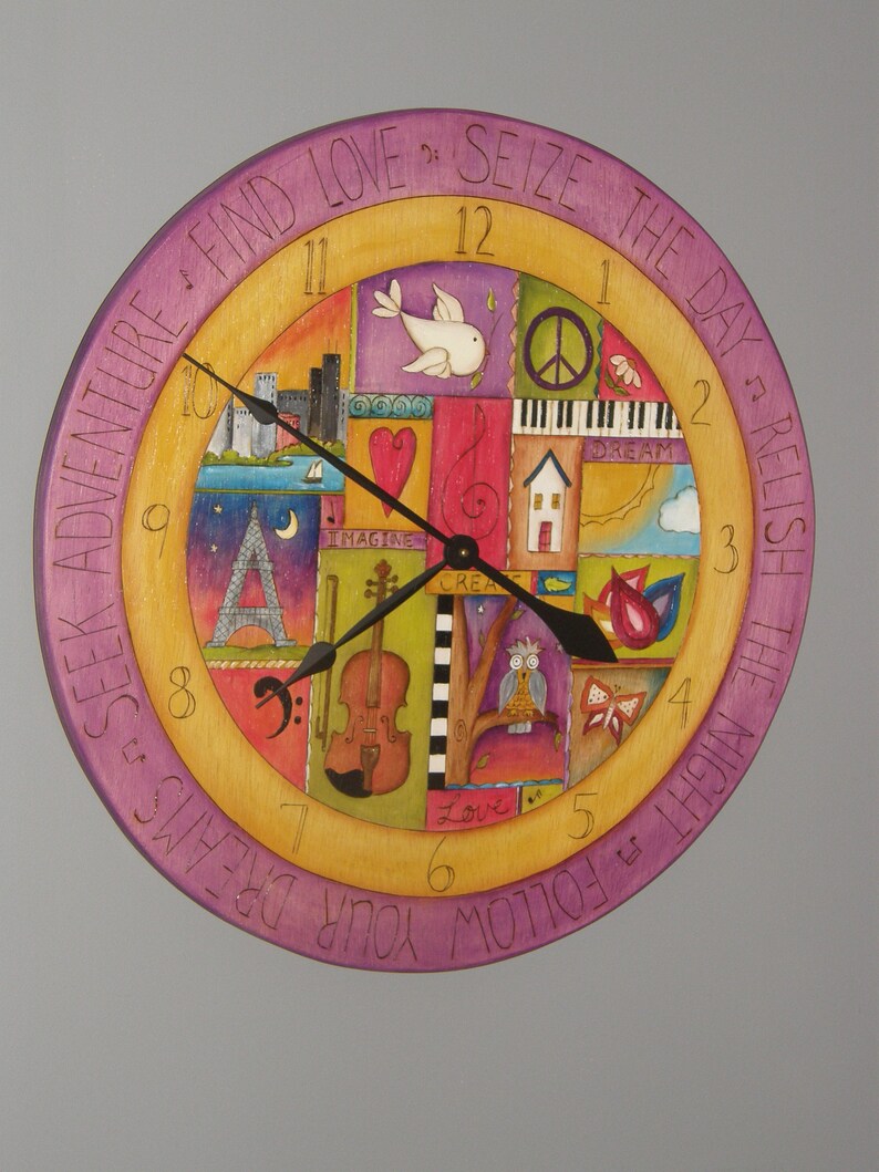 May include: A colorful wooden clock with a purple outer ring and a yellow inner ring. The clock face is decorated with various images, including a bird, a piano, a house, a violin, and an owl. The clock hands are black and the numbers are in white. The outer ring has the text "SEEK ADVENTURE FIND LOVE? SEIZE THE DAY? RELISH THE NIGHT? FOLLOW YOUR DREAMS".