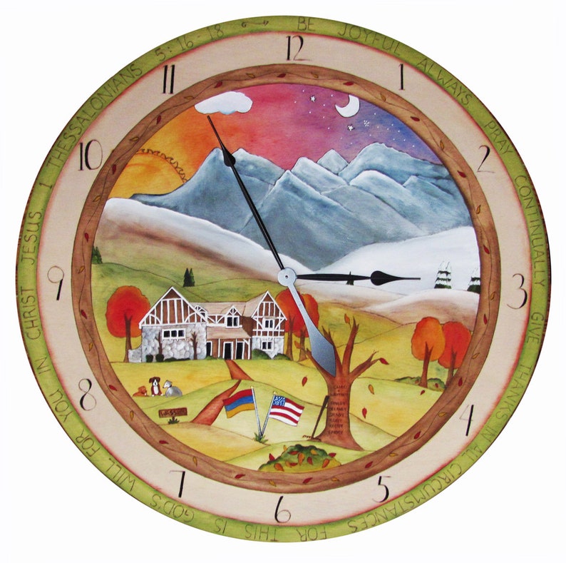 May include: A round wooden clock with a painted scene of a house in a mountain landscape. The clock face has Roman numerals and the words "Be Joyful Always Pray Continually Give Thanks In All Circumstances" around the edge. The clock hands are pointing to 12:00.