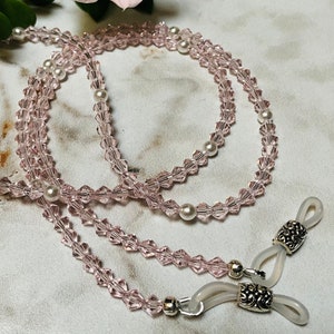 May include: A pink crystal and pearl beaded eyeglass chain with silver tone clasps. The chain is made of small pink crystal beads and larger white pearl beads.